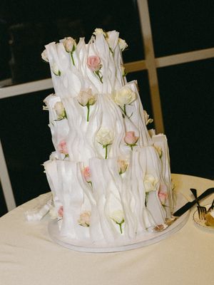 Elegant three-tier white wedding cake adorned with pink and cream roses, featuring textured ruffled fondant design.