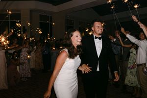 Bride and groom walk through sparkler exit surrounded by cheering wedding guests at elegant evening reception.