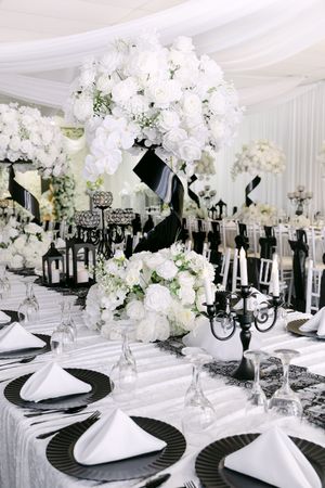 Elegant black and white wedding reception table with white floral centerpieces, candelabras, and neatly folded napkins.