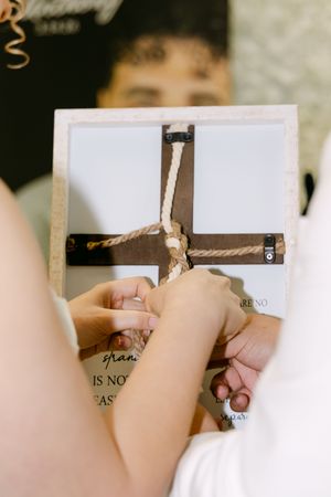 Hands tying a rope around a wooden cross during a wedding unity ceremony.