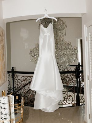 Elegant white satin mermaid wedding dress hanging on a hanger in a luxurious venue with crystal chandelier.