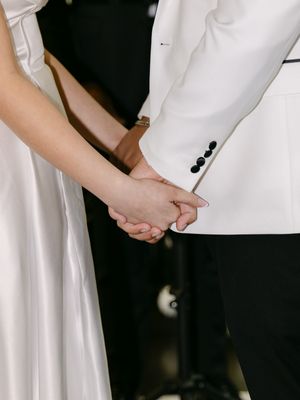 A bride and groom holding hands at the altar, wearing white wedding attire during their ceremony.