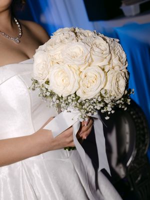 Bride in white strapless gown holding elegant bouquet of white roses and baby's breath with white ribbon.