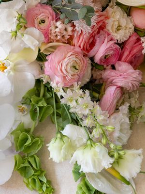 Lush arrangement of pink ranunculus, white orchids, and green hydrangeas on a soft pastel background.