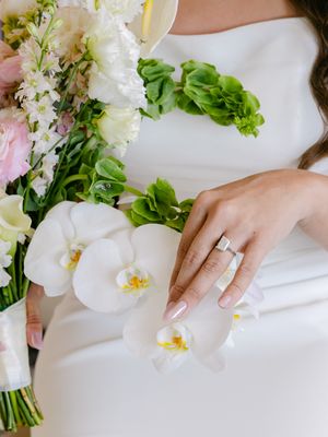 Bride holding a lush wedding bouquet with white orchids and pink flowers, showcasing an elegant diamond engagement ring.