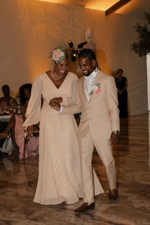 Elegant couple in matching champagne outfits share a dance at a wedding reception on a marble floor.