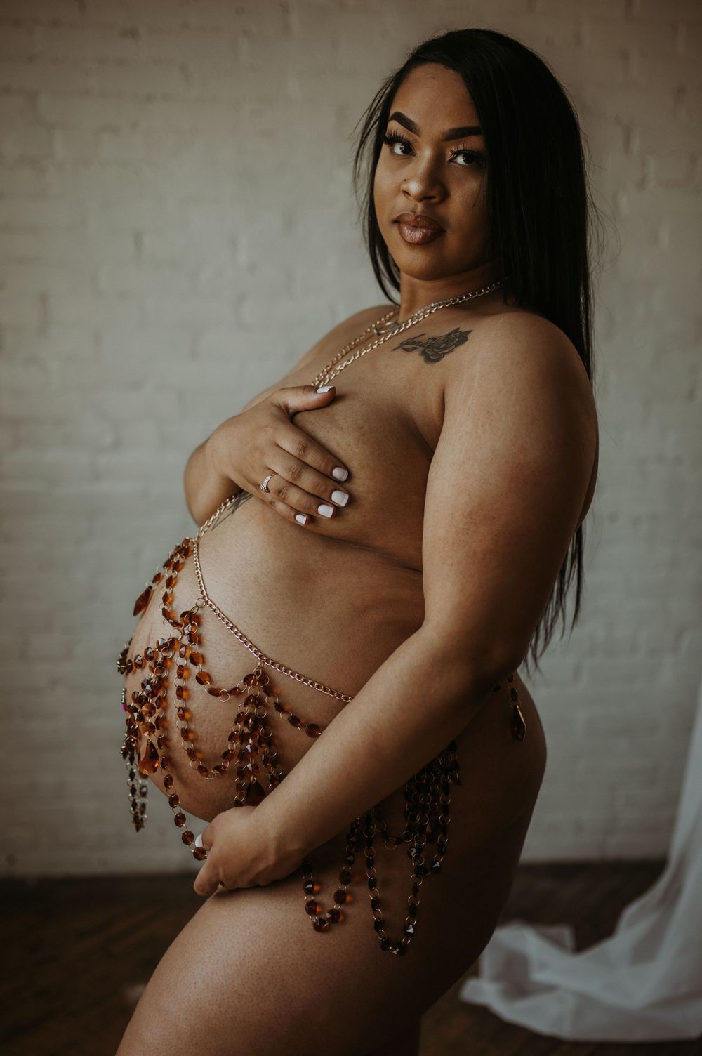 Pregnant Black woman wearing decorative amber bead chains poses in bright studio.