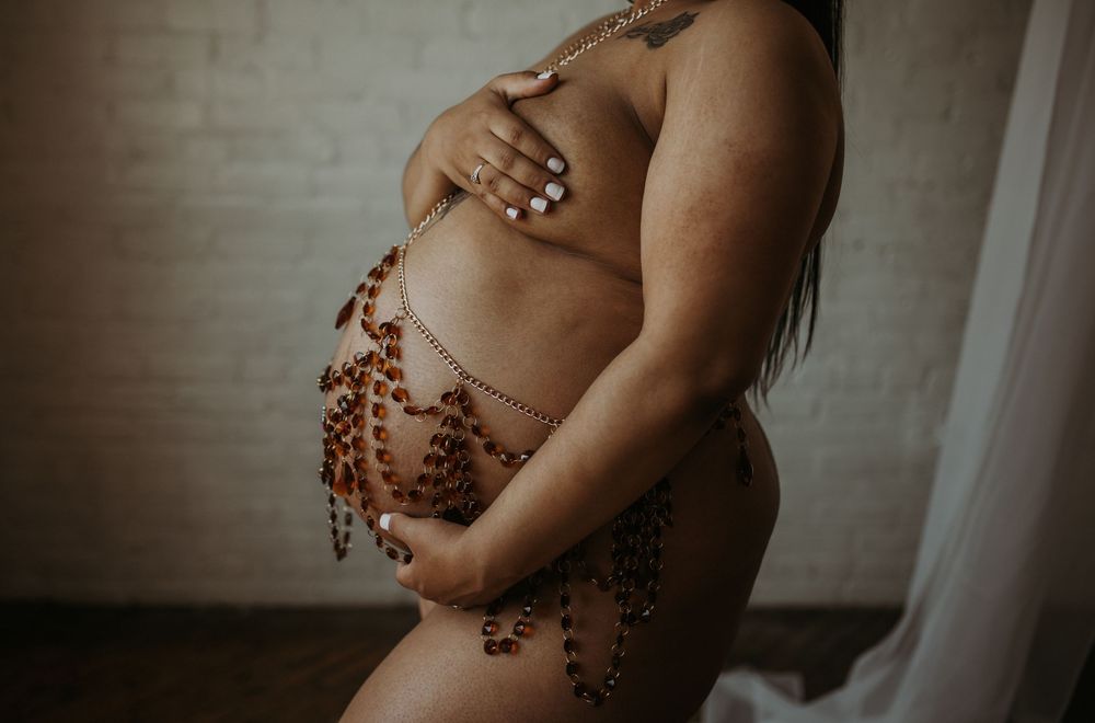 Close-up of pregnant belly adorned with decorative amber beaded body chains.