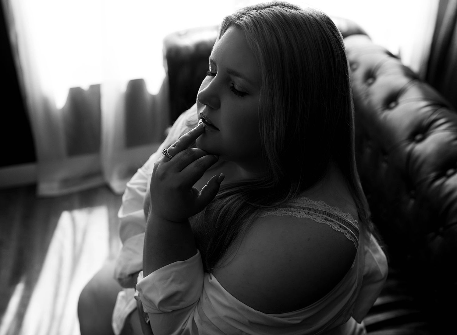 woman in white button down sits on couch with fingers on lips after learning what you need to know about boudoir
