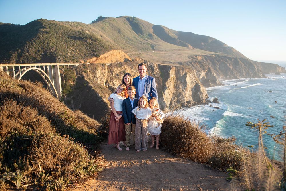 Family poses together at Bixby Creek Bridge overlook in Big Sur, California with stunning coastal views.