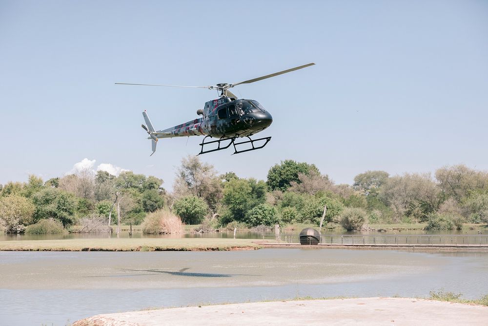 Black helicopter flying low over a river surrounded by lush green trees on a clear day. Palala Boutique Game Lodge & Spa.