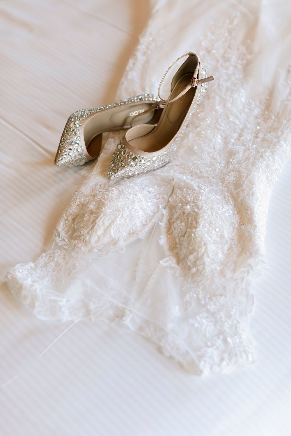 Sparkling silver crystal bridal heels resting on a white lace wedding dress on a bed. Palala Boutique Game Lodge & Spa.