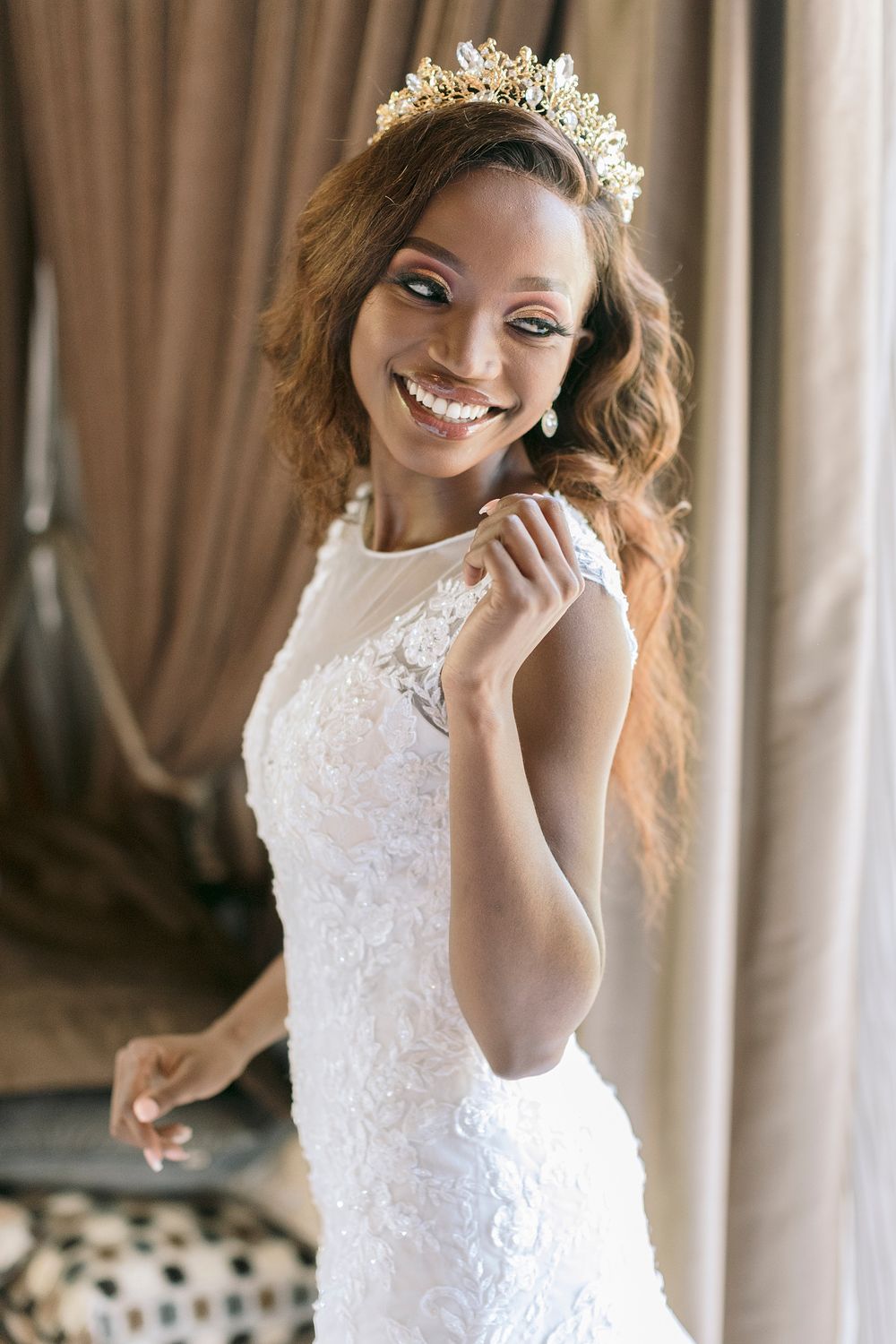 Smiling Black bride in white lace gown and gold crown poses elegantly indoors. Palala Boutique Game Lodge & Spa.
