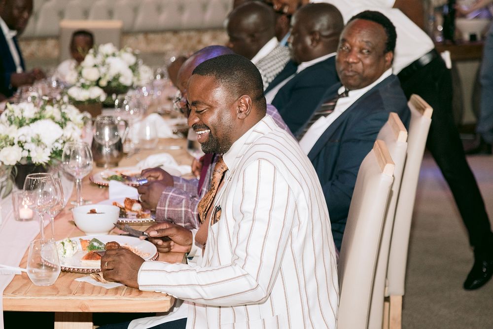 Guests smile and laugh at an elegant wedding reception dinner table with white floral centerpieces. Palala Boutique Game Lodge & Spa.