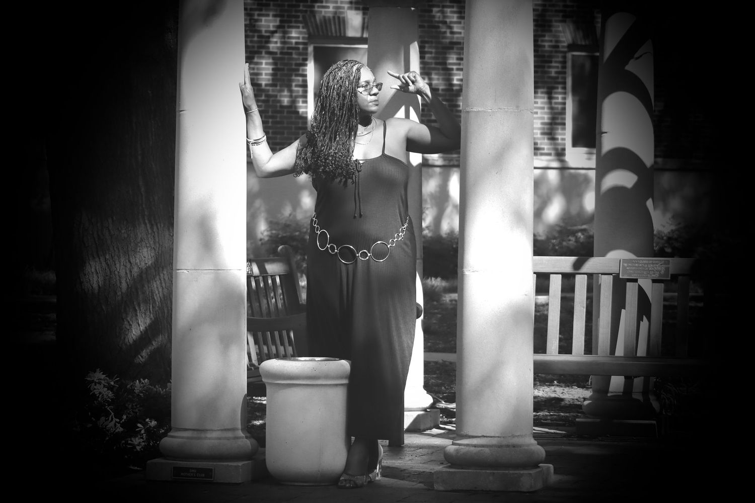 Black and white photo of a woman in a black dress posing between columns on a porch.