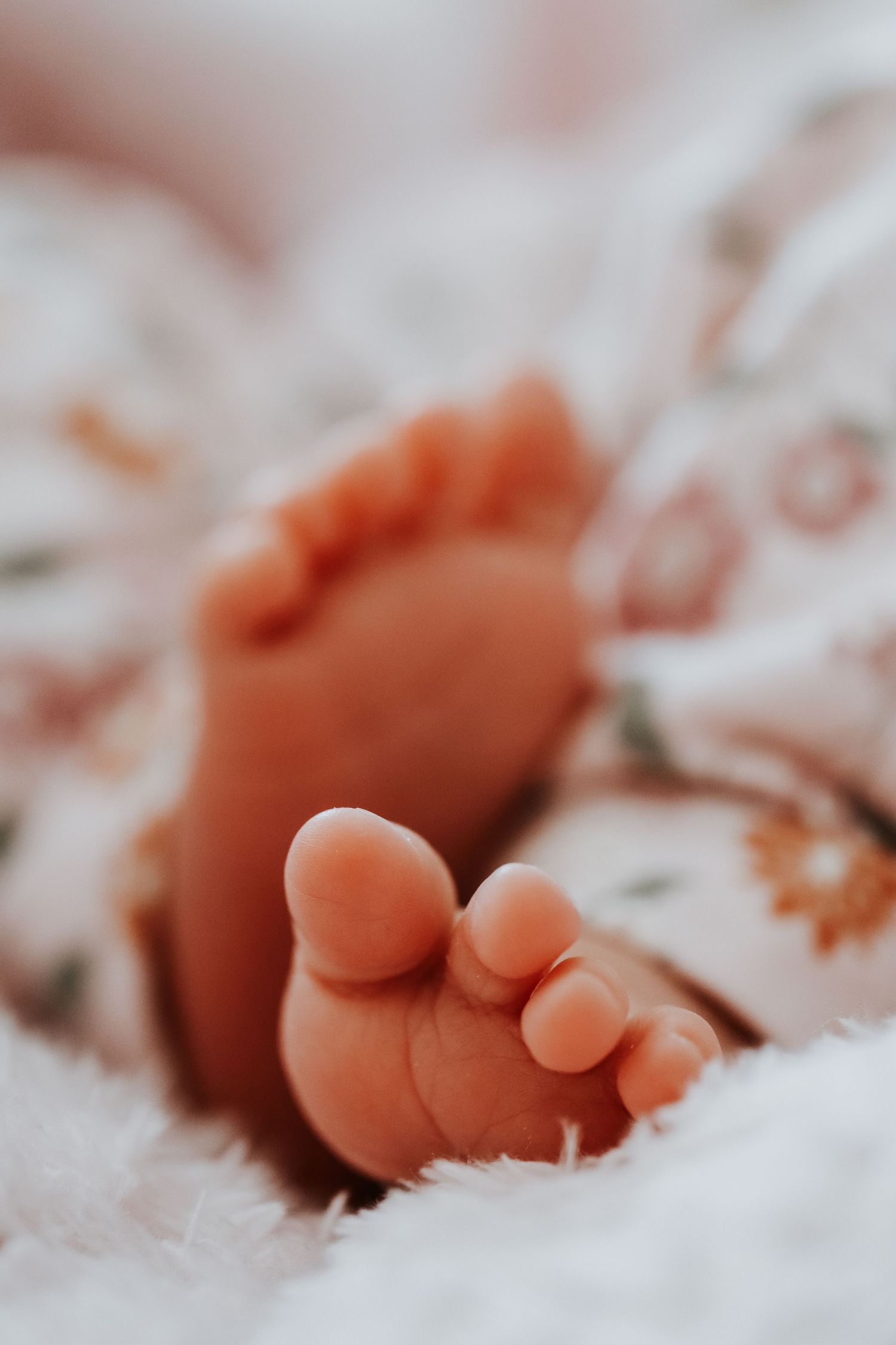 Close-up of tiny newborn baby feet resting on a soft white blanket with floral pattern clothing.