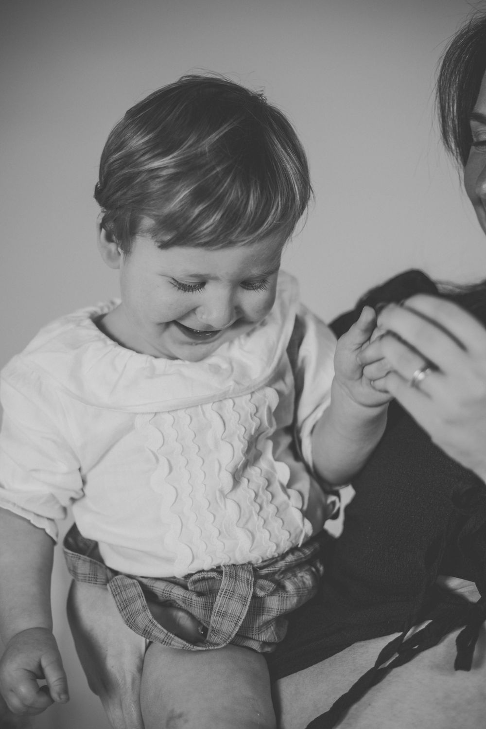 Black and white photo of a happy toddler smiling while being held by an adult wearing a ring.