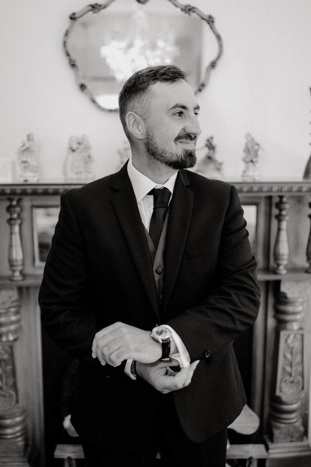 Black and white portrait of smiling groom adjusting cufflinks before wedding ceremony.