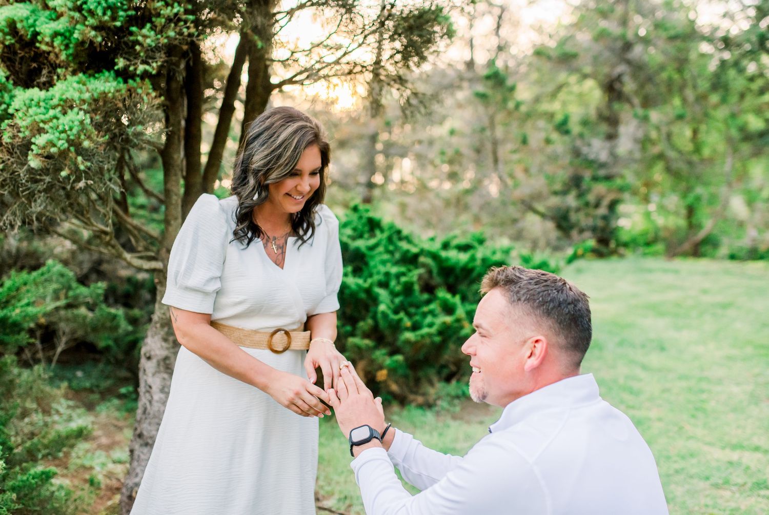 Man on one knee placing engagement ring on womans finger in romantic outdoor garden proposal.