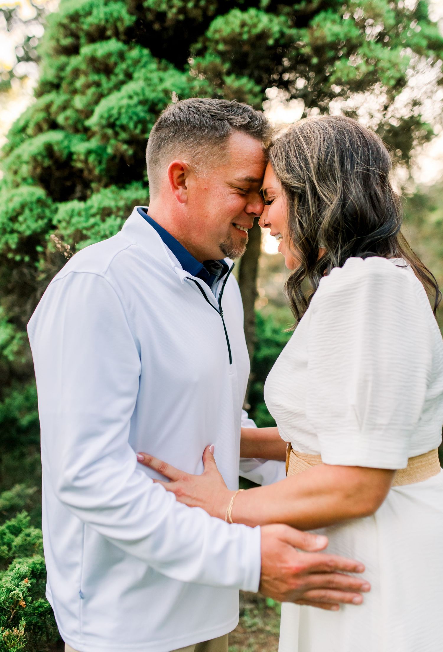 Romantic couple sharing an intimate forehead-to-forehead moment outdoors surrounded by green trees.