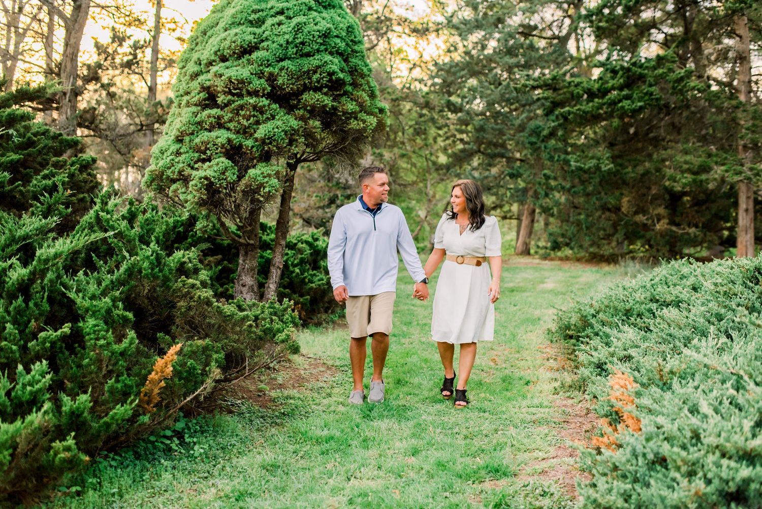 Happy couple walking hand in hand through a scenic garden path surrounded by lush green trees.
