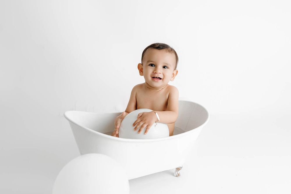 Affordable photographer Menifee photo of smiling baby sitting in a white mini bathtub against a clean white background.