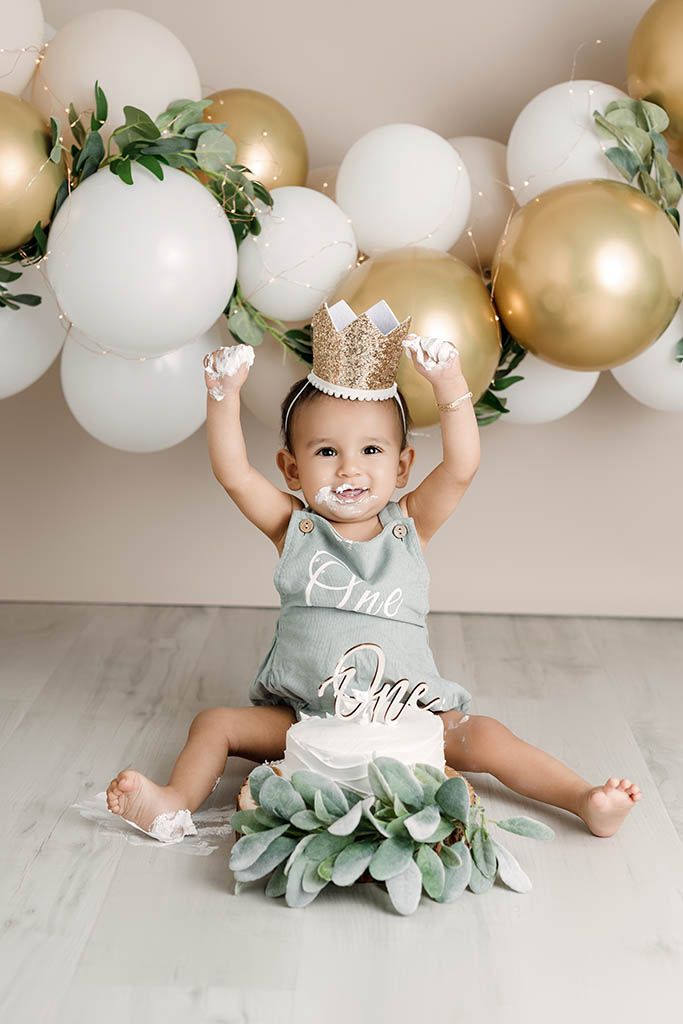 Baby's first birthday cake smash with gold crown, balloons, and sage green romper.
