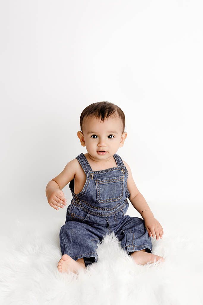 Affordable photographer Menifee photo of baby in denim overalls sitting on a fluffy white rug.