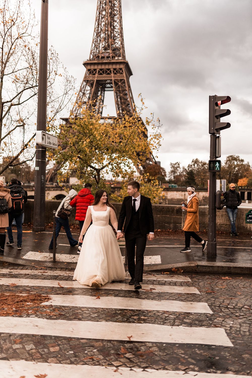 Wedding couple crosses zebra crossing hand in hand with Eiffel Tower in background.