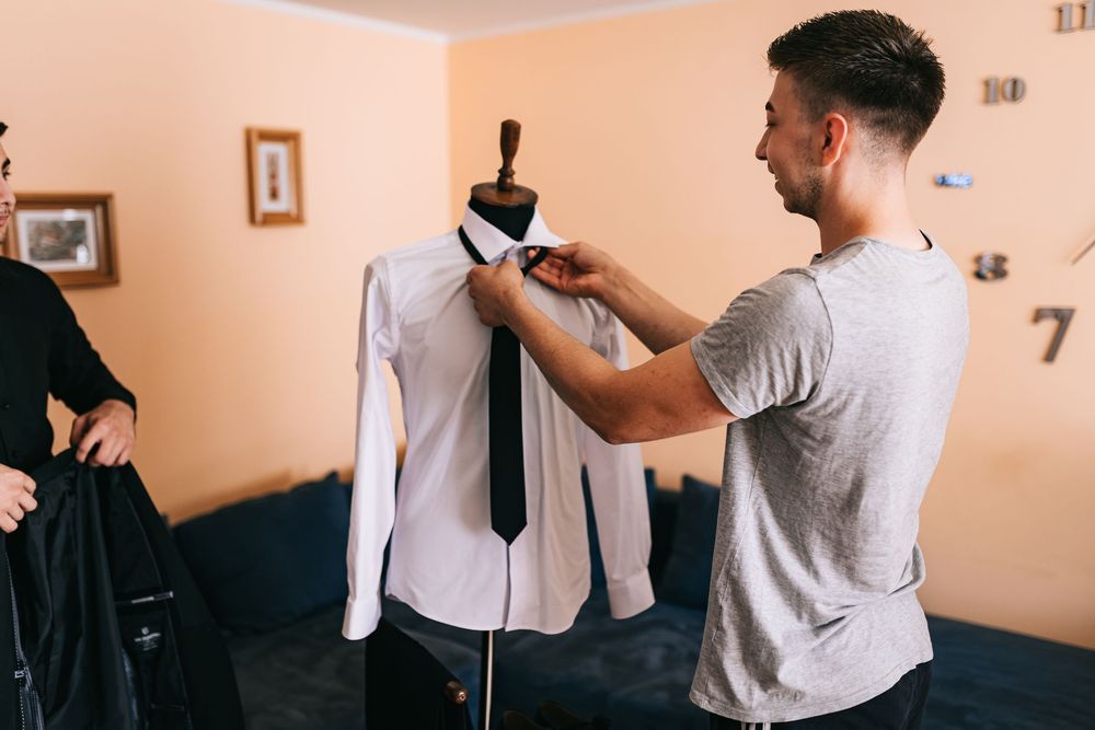 Groom preparing wedding attire, adjusting tie on mannequin in hotel room.