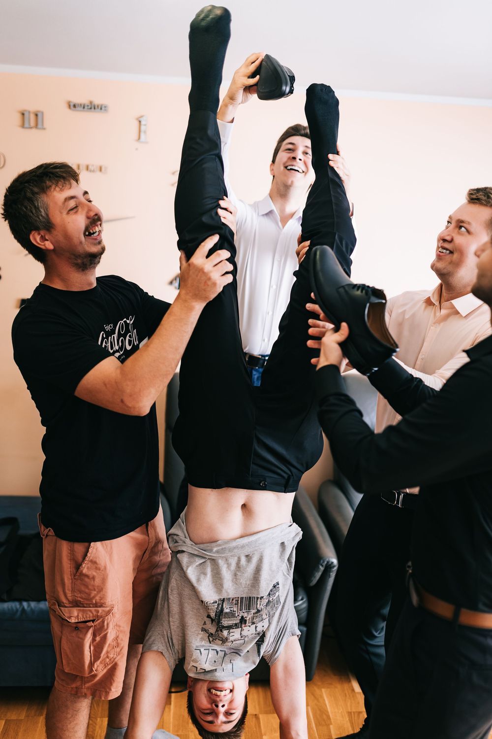 Groomsmen playfully lifting groom upside down during fun pre-wedding celebration.