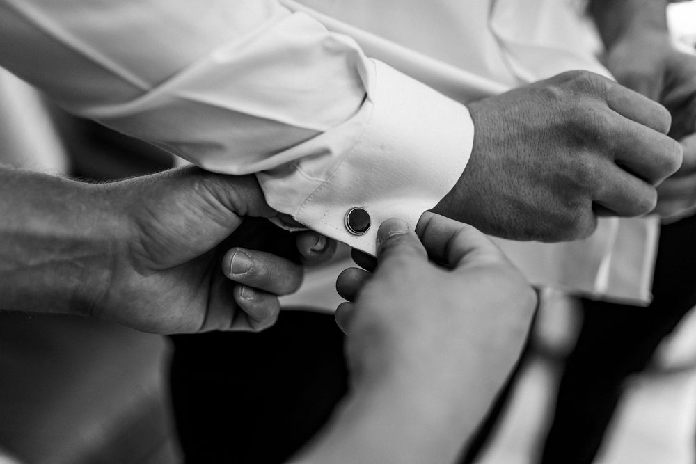 Black and white close-up of hands fastening silver cufflinks on white dress shirt sleeve.