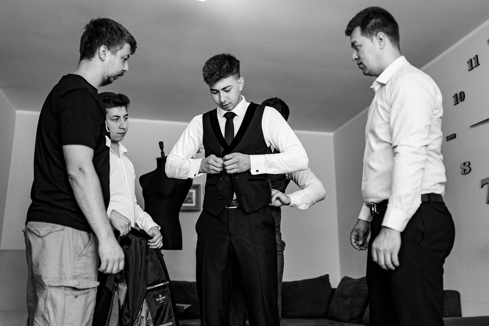 Black and white photo of groom and groomsmen helping each other get dressed for wedding.