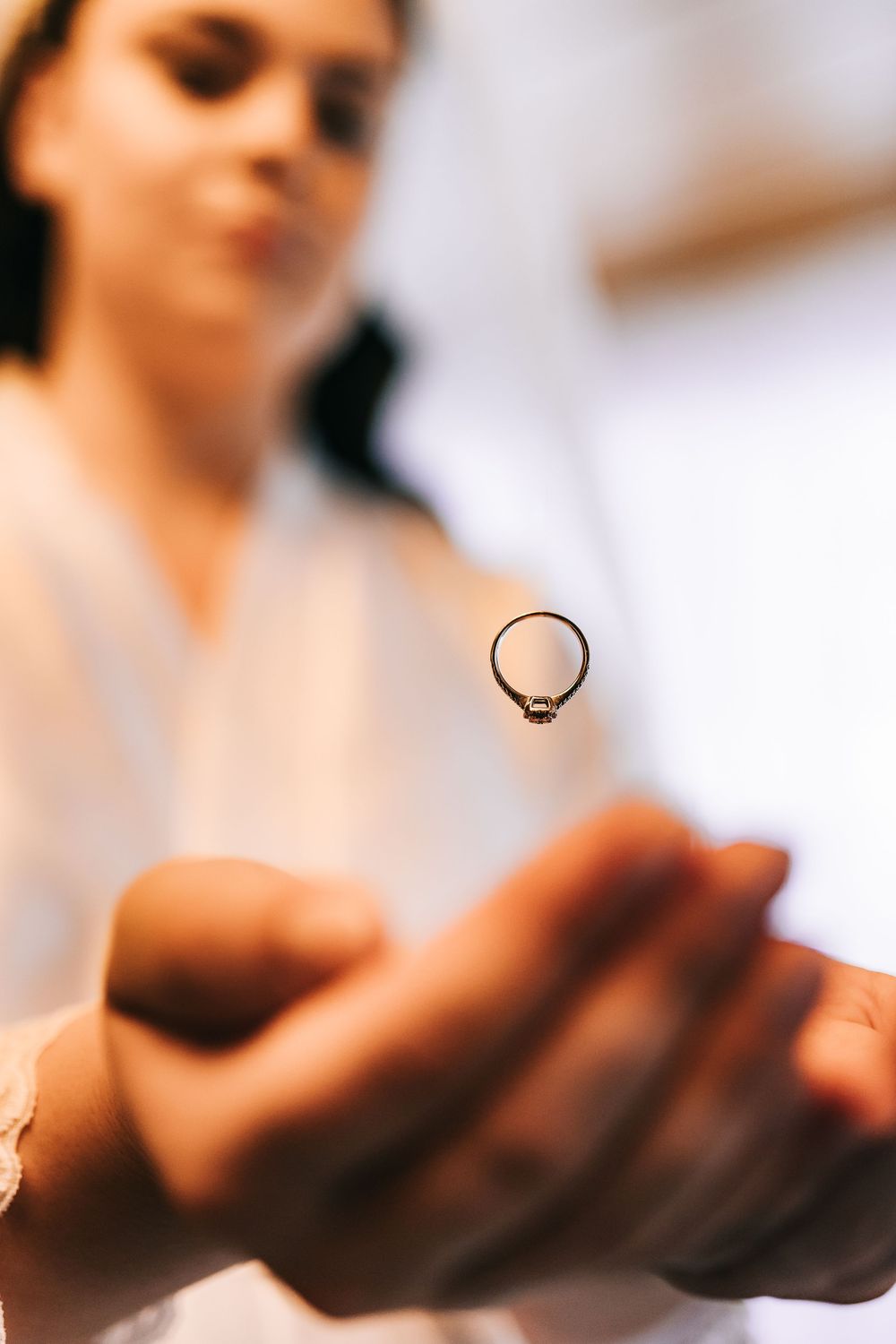 Close-up of elegant diamond engagement ring being held up by bride in white robe.