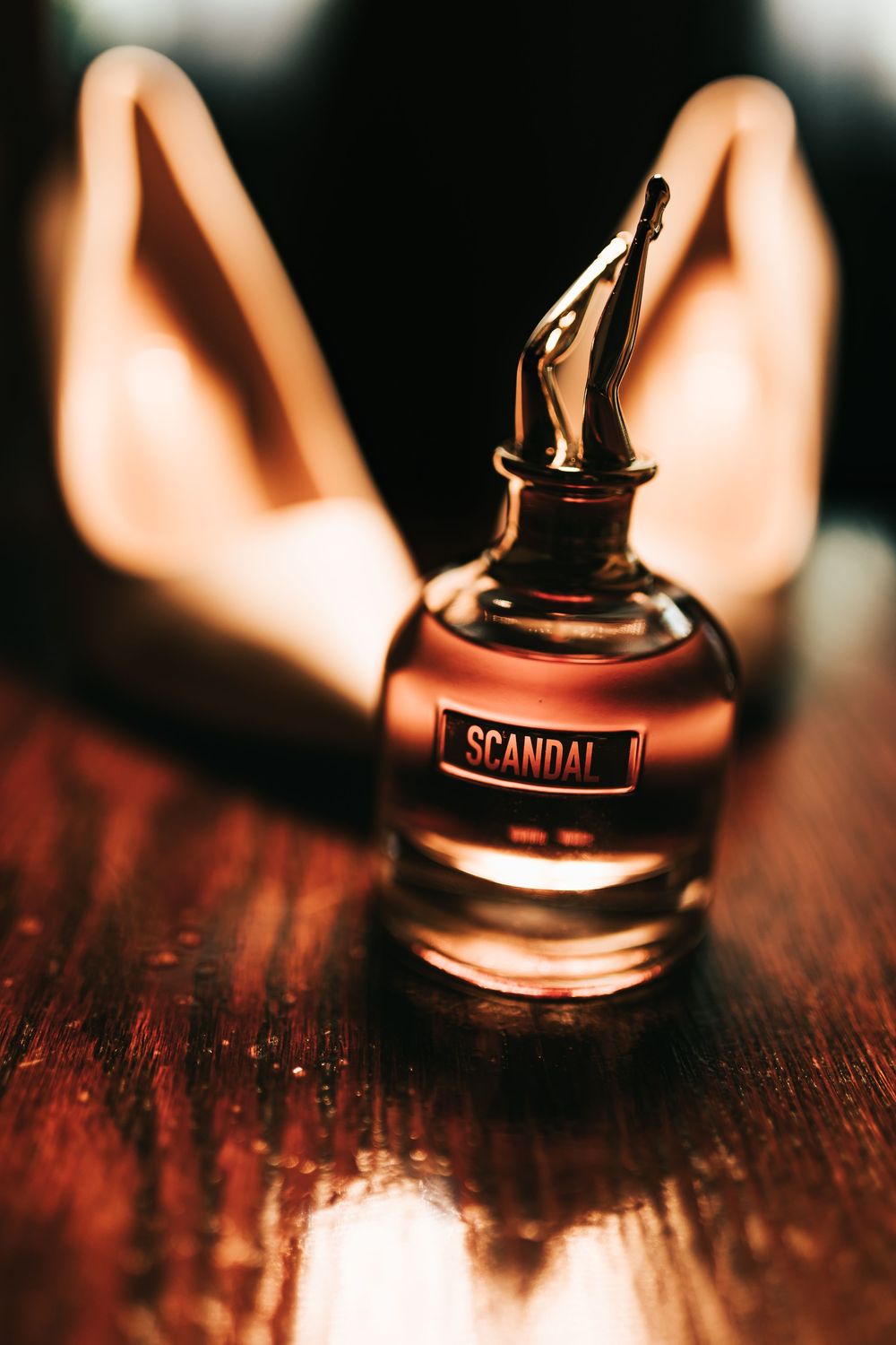 Jean Paul Gaultier Scandal perfume bottle displayed on a wooden surface with warm ambient lighting.