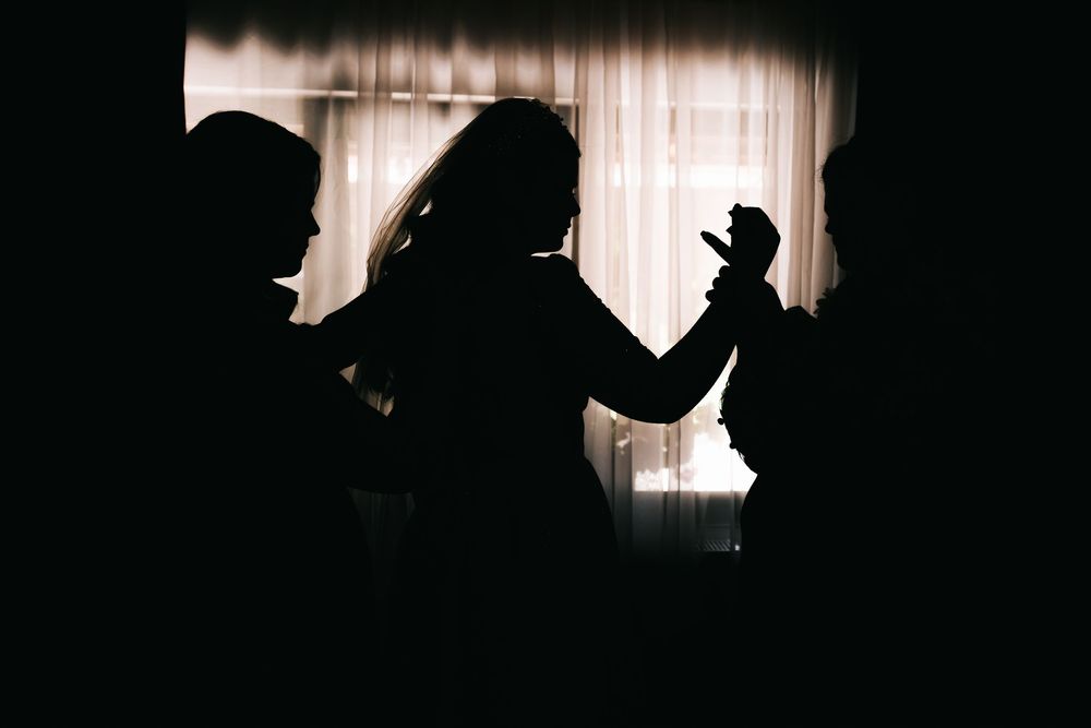 Silhouettes of people against a bright window, bride in wedding dress holding flowers.