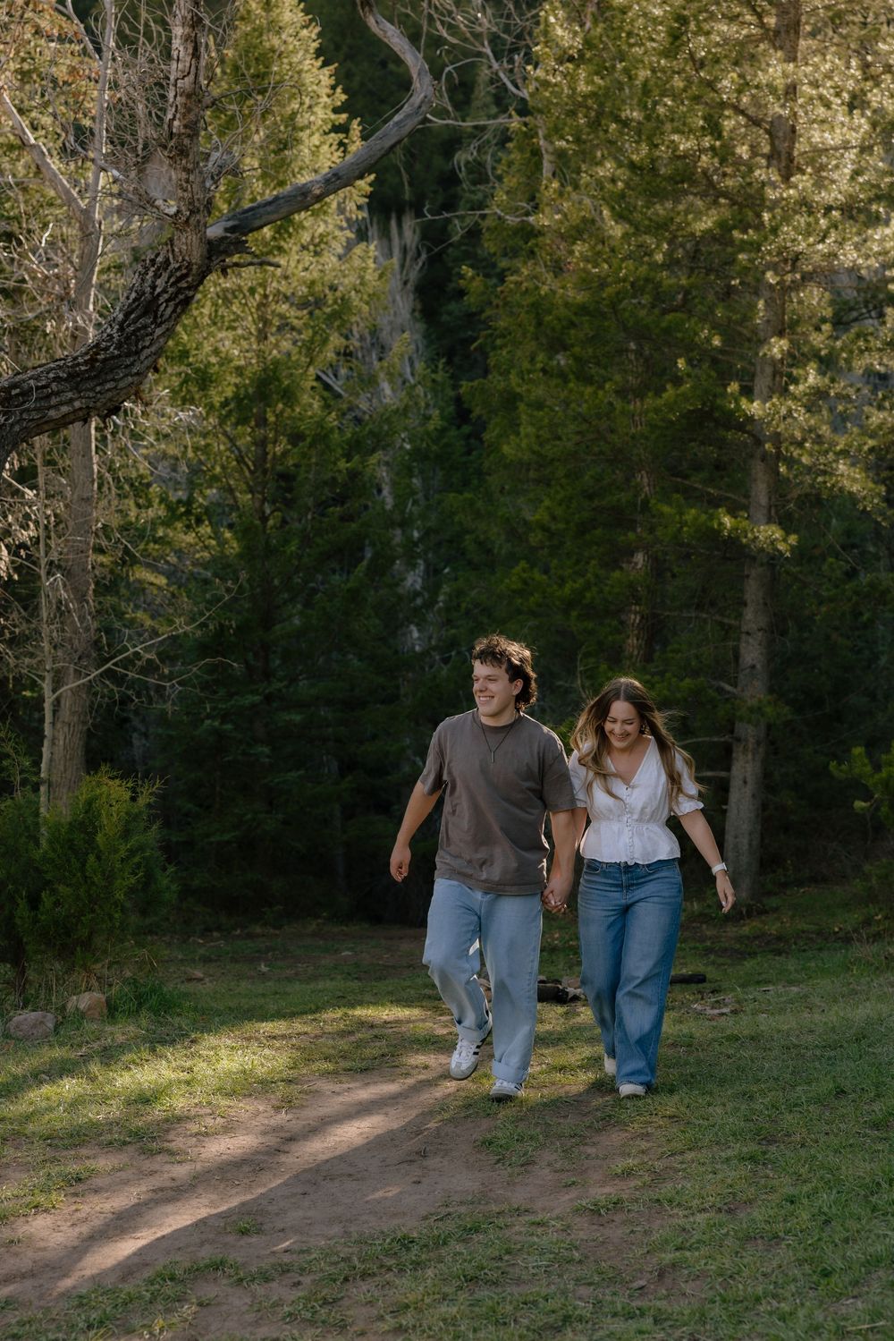 Happy couple holding hands and walking together through a sunny forest clearing.