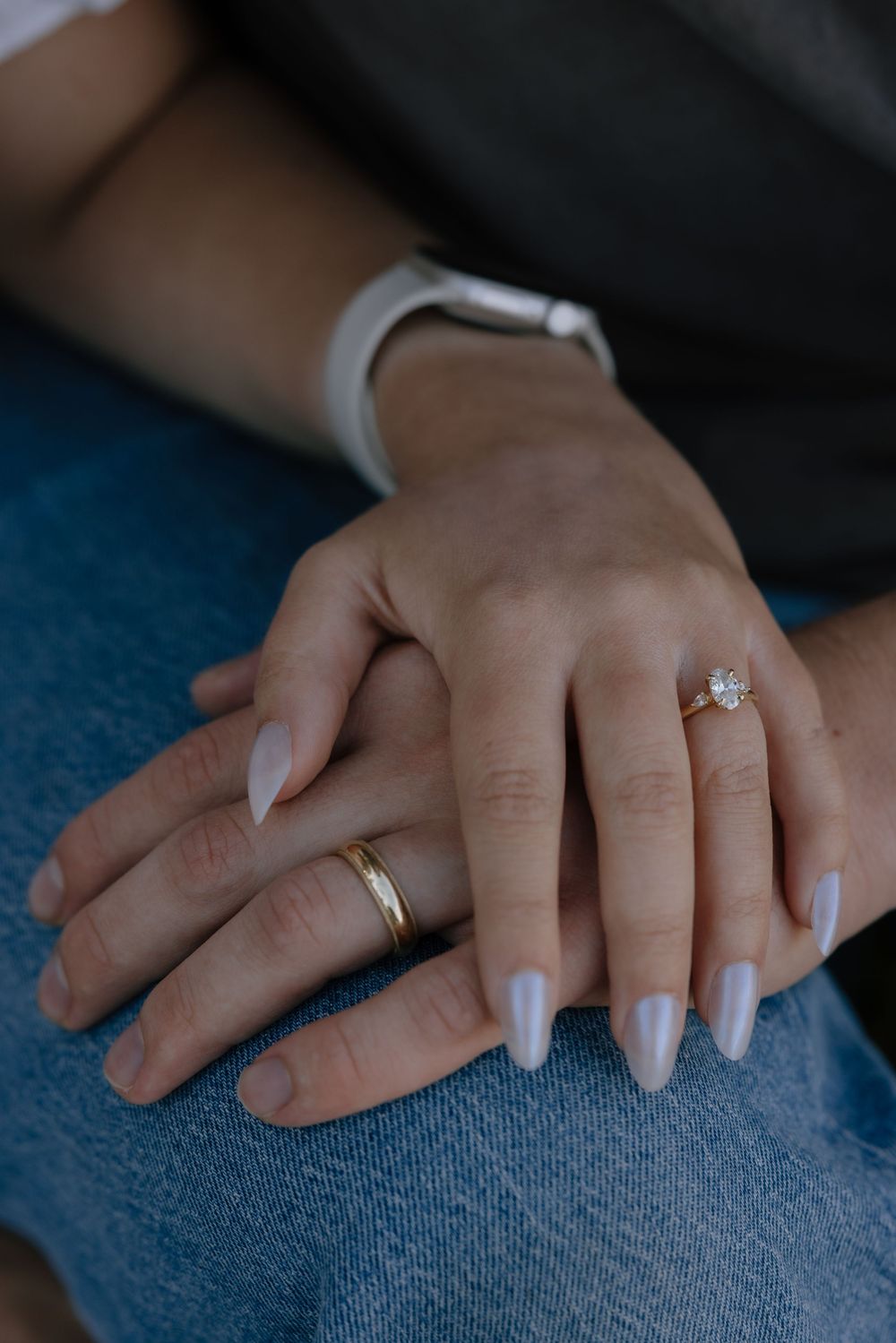 Close-up of engaged couples hands showing diamond engagement ring and gold band with white manicure.