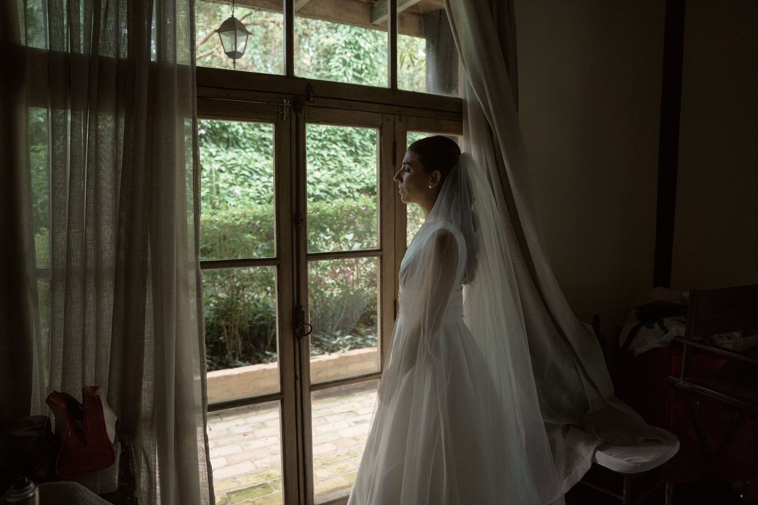 Woman in white lace robe sitting elegantly, holding a small clutch purse in a softly lit room.