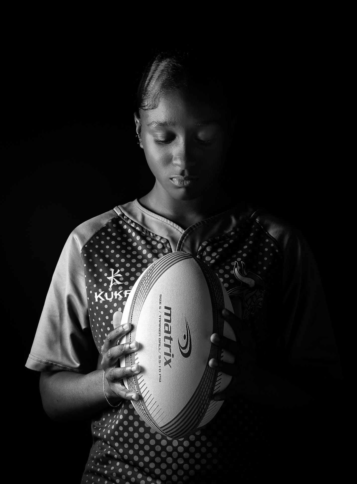 A black and white image of a girl looking down and holding a rugby ball