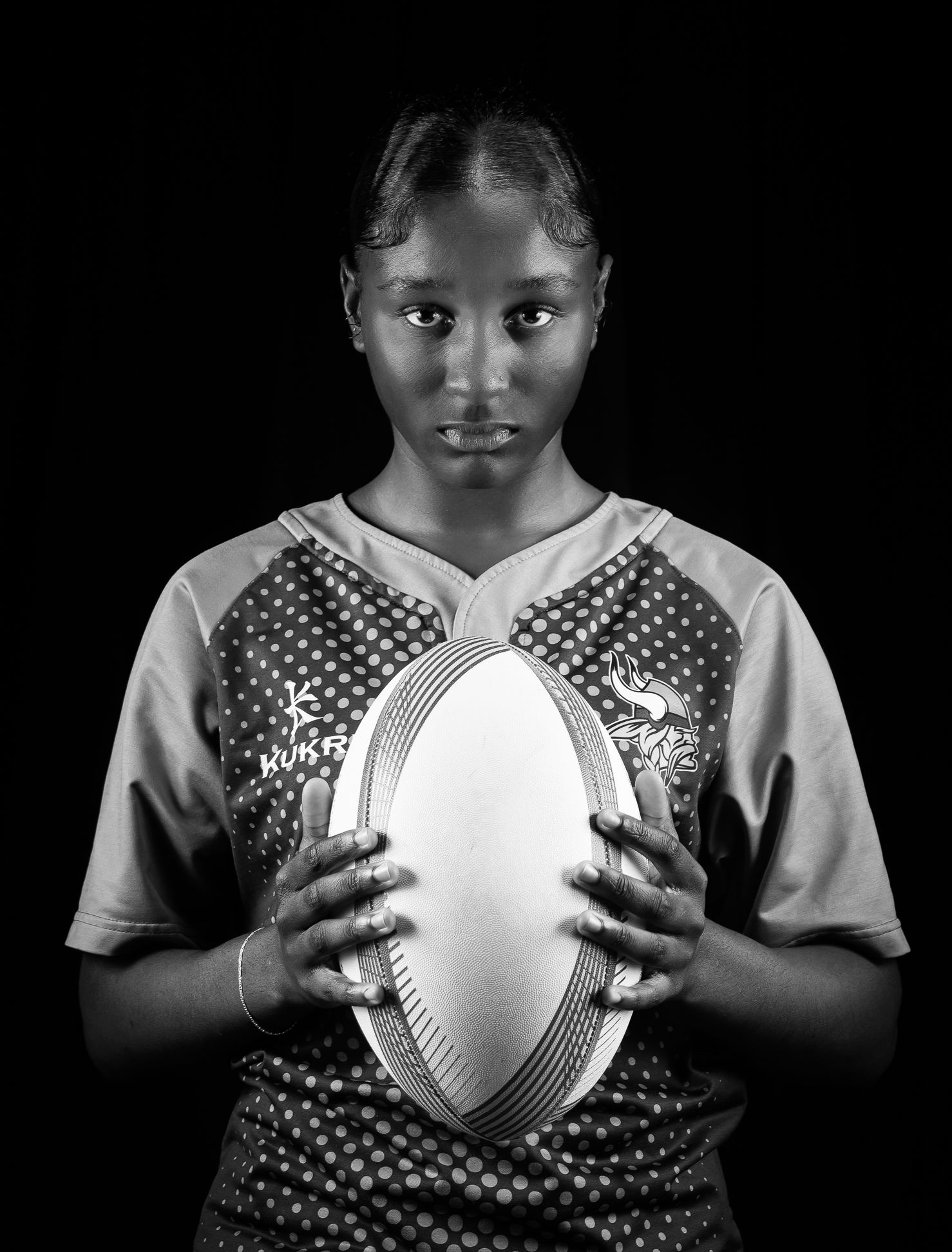 A black and white image of a girl holding a rugby ball, looking up at the camera