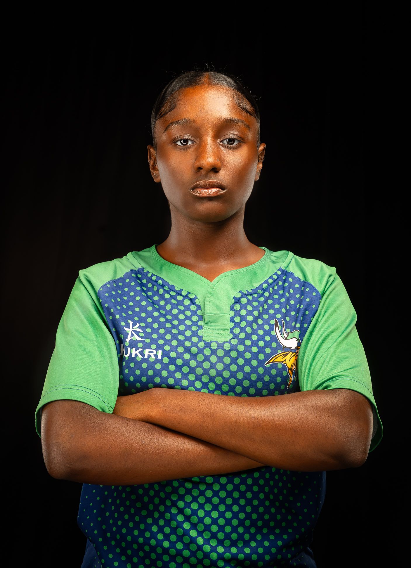 An image of a girl in a green rugby jersey with her arms crossed in front of her chest, looking straight at the camera