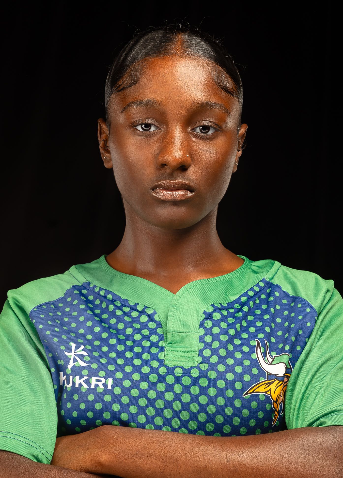 An image of a girl in a green rugby jersey with her arms crossed in front of her chest, looking straight at the camera, closer shot