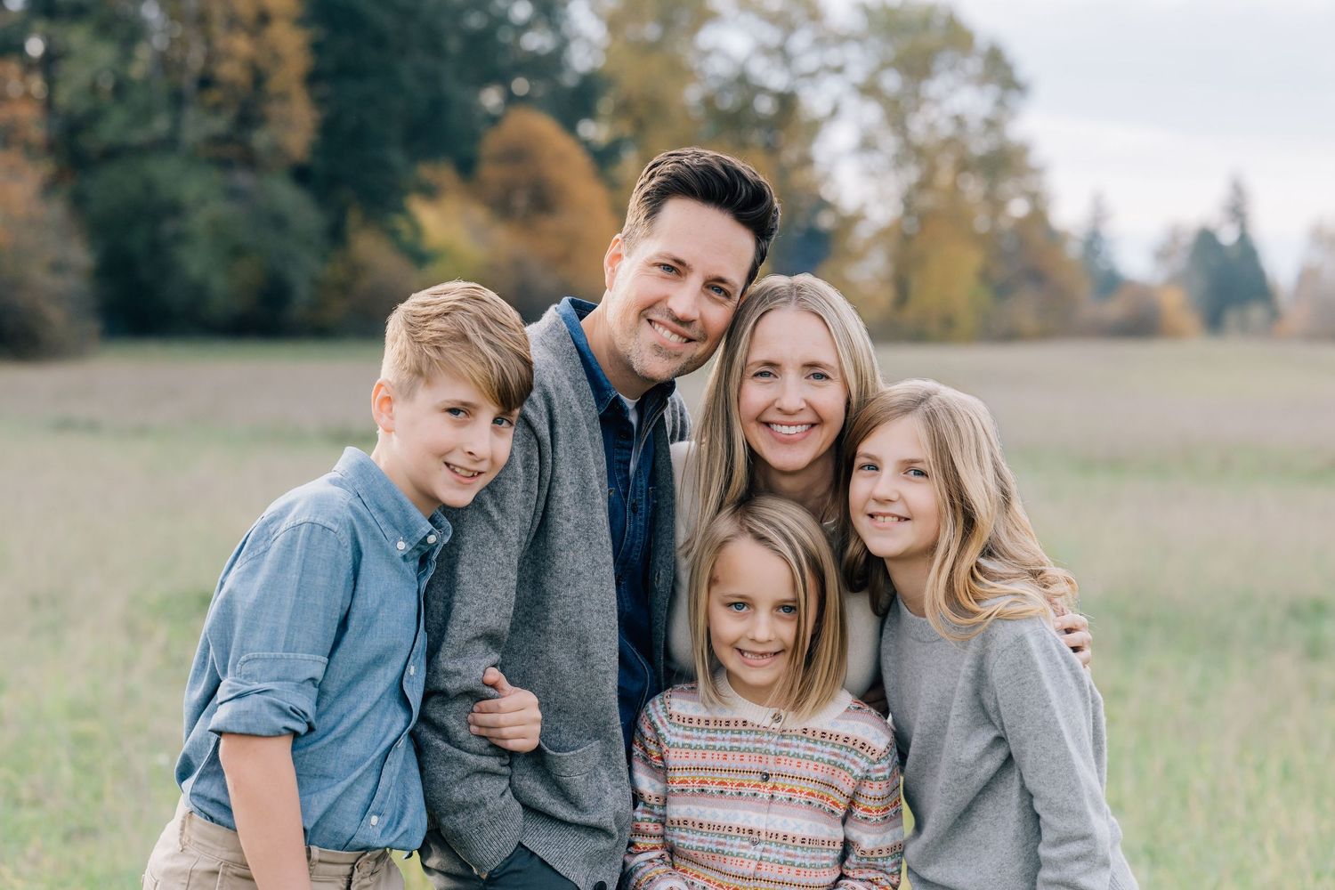 Happy family of five smiling together in an autumn field, parents with three children in coordinated outfits.