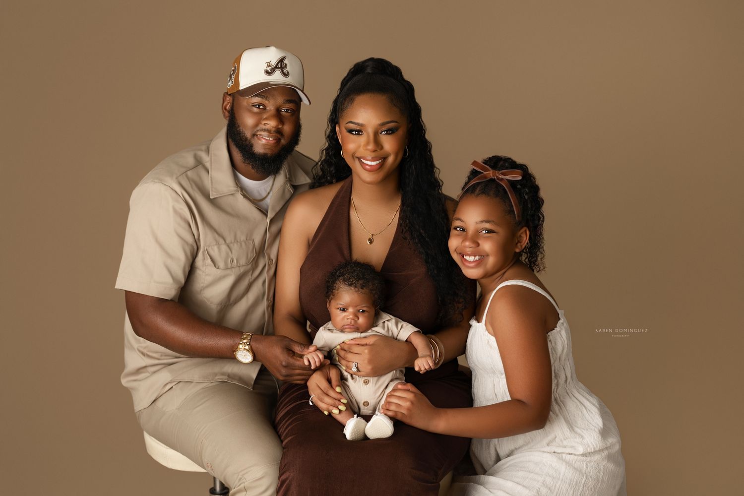 A joyful family of four poses for a professional portrait, with parents holding their newborn and young daughter smiling warmly.