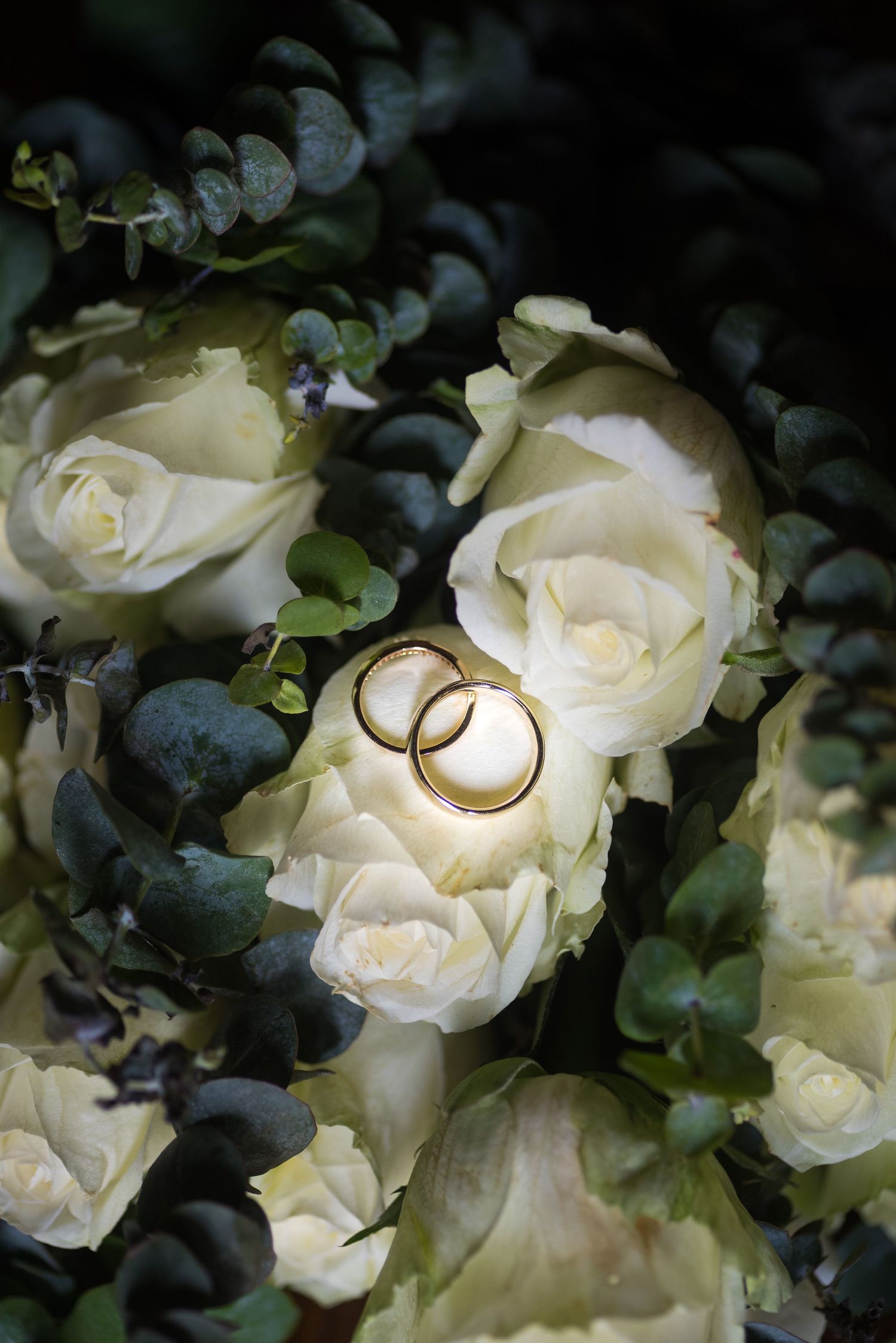 Two gold wedding rings rest on white roses and eucalyptus in a bridal bouquet.