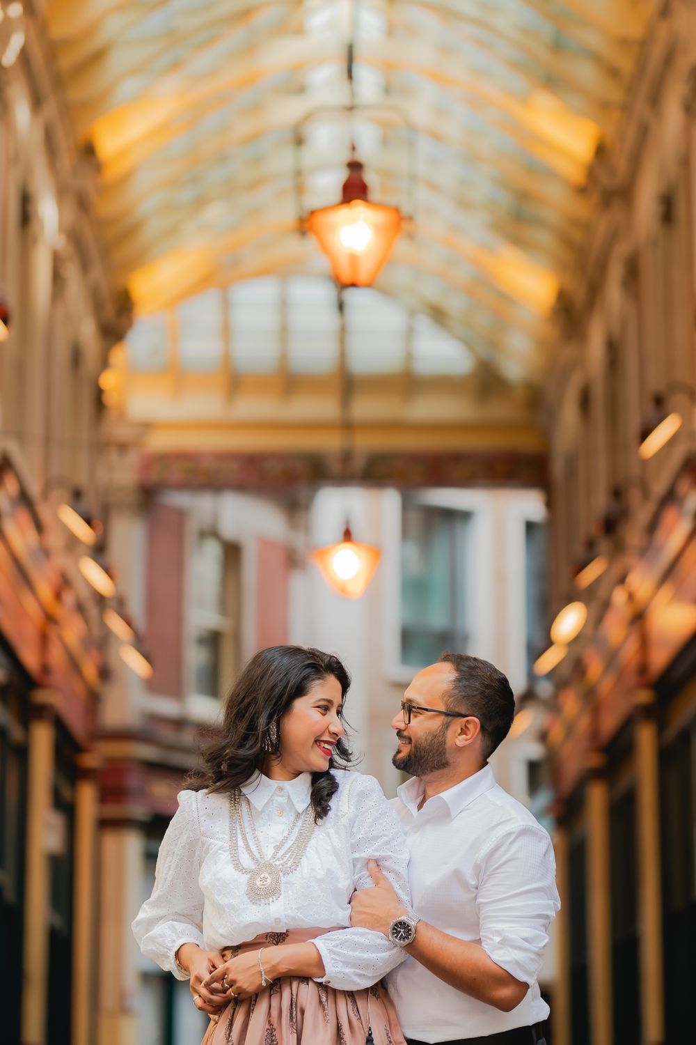 Couple sharing a romantic moment in a elegant Victorian arcade with warm glowing lanterns overhead.