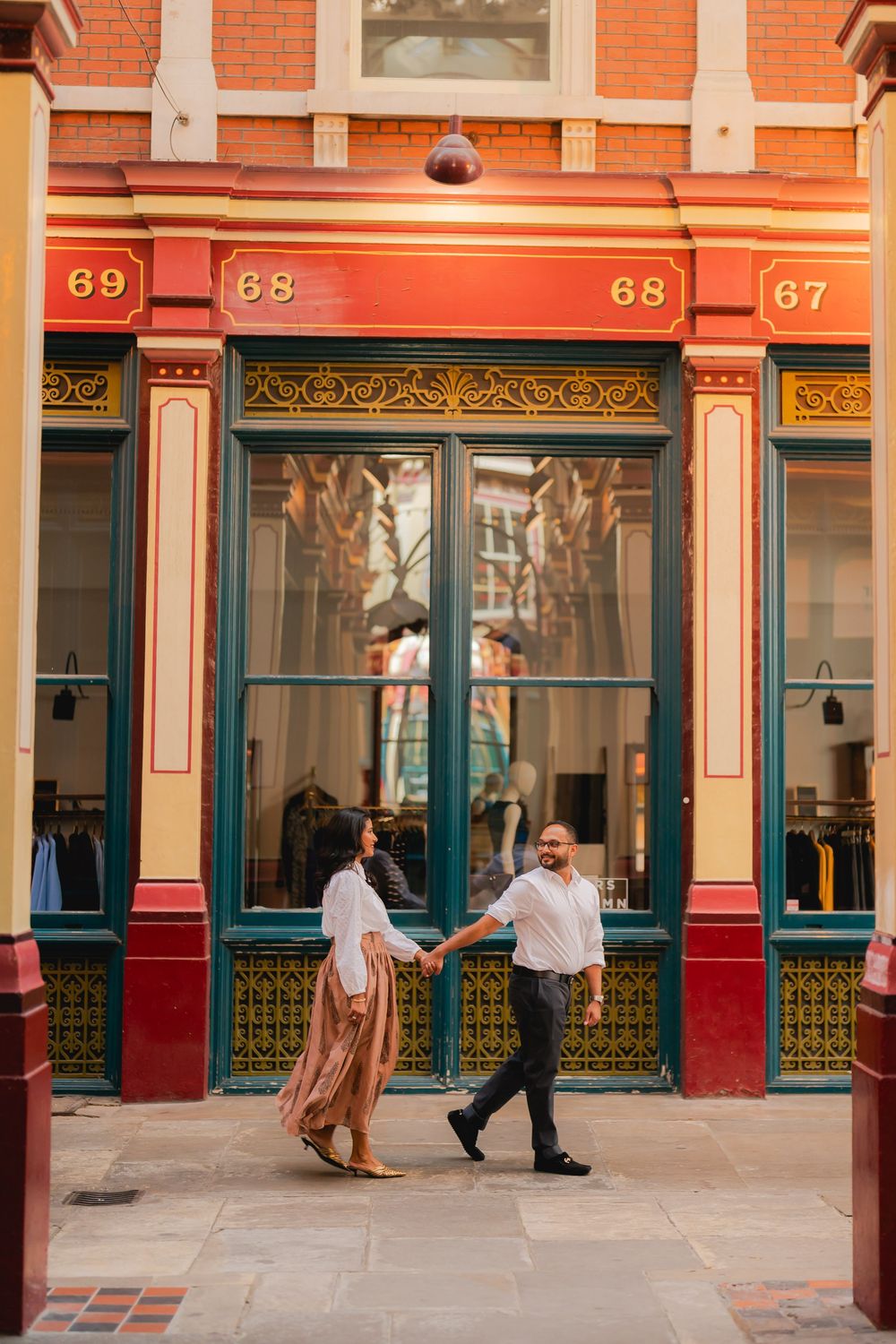 Couple holding hands walking past a vibrant red and green Victorian shopfront at Leadenhall Market, London.