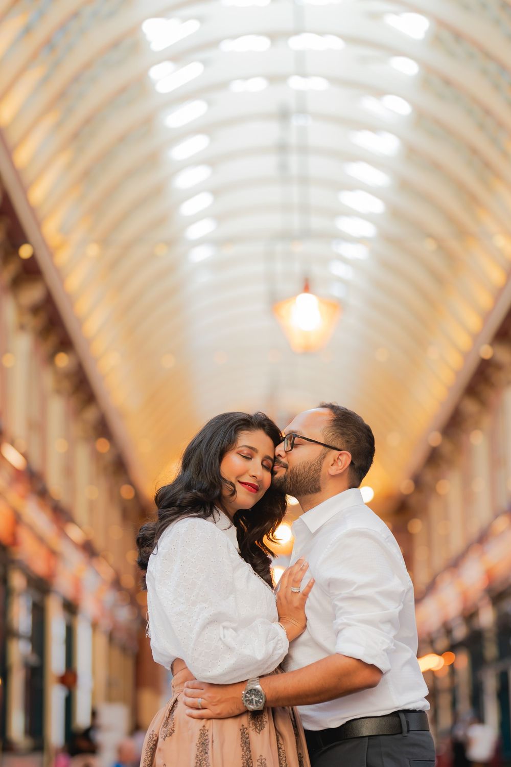 Couple sharing a romantic embrace and kiss in a beautiful arched gallery with warm glowing lights.