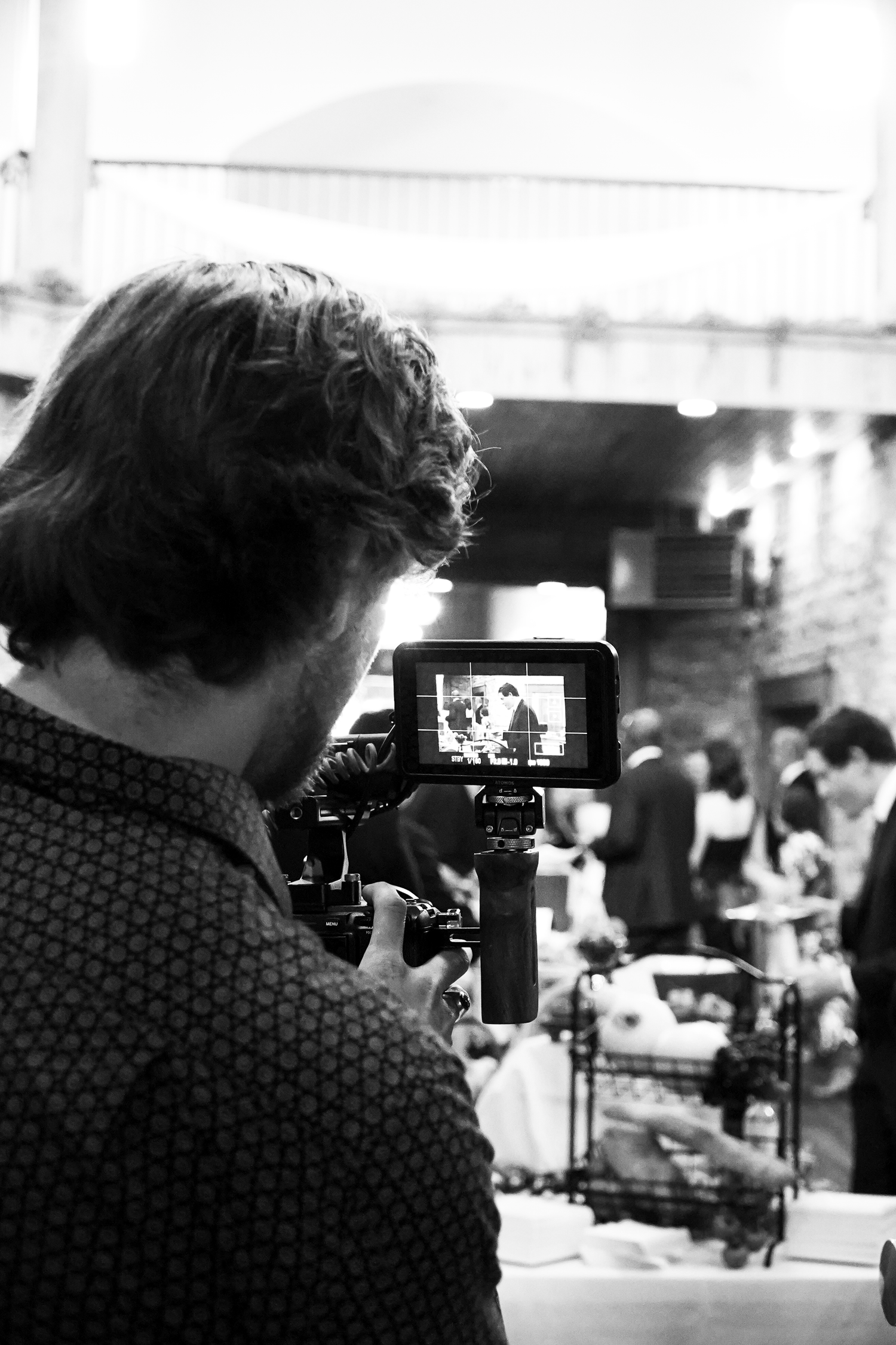 Black and white photo of a videographer filming a wedding reception on a camera with an external monitor.